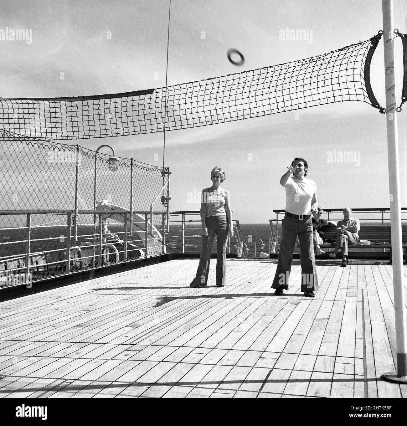 1960s, historisch, Deck-Tennis auf dem Sagafjord-Schiff, draußen auf dem Deck des Schiffes, ein Mann und eine Frau spielen ein Spiel mit dem Werfen über ein Netz aus einem Gummiring, ein Hybrid aus Tennis und Quoits und so ist es auch bekannt als Ring-Tennis, tennikoit oder tenniquoits. Stockfoto