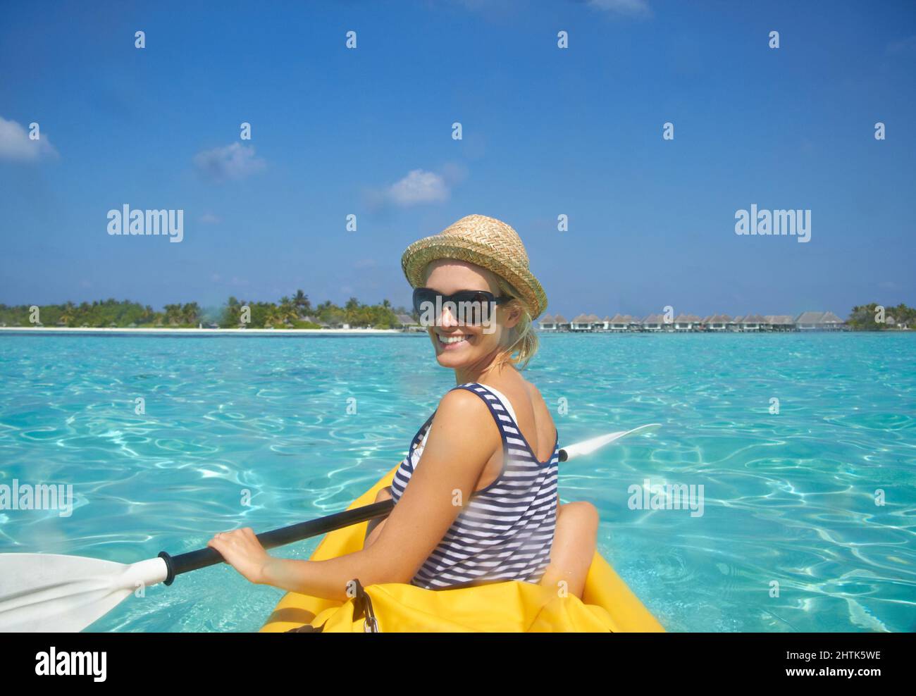 Paddeln zum Strand. Eine schöne junge Frau, die auf einem Boot in einem tropischen Ozean paddelt. Stockfoto