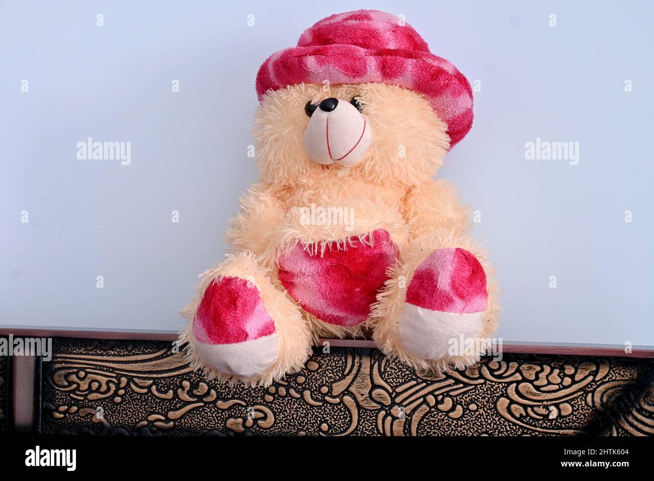 Nahaufnahme des wunderschönen rosa braunen Teddybären, der auf einem braunen Tisch über einem weißen braunen Hintergrund sitzt. Stockfoto