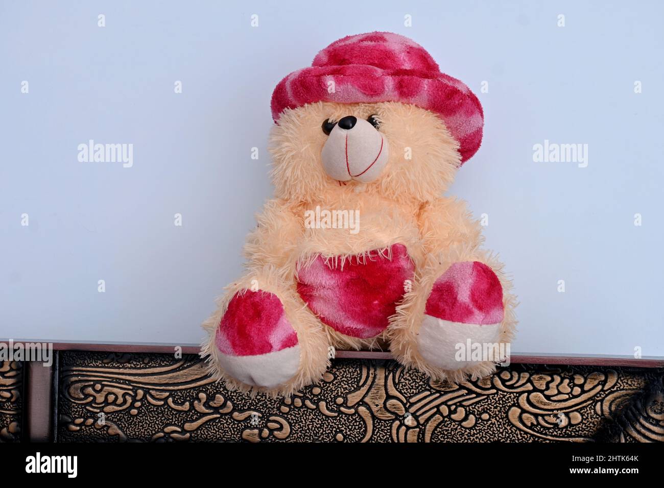 Nahaufnahme des wunderschönen rosa braunen Teddybären, der auf einem braunen Tisch über einem weißen braunen Hintergrund sitzt. Stockfoto