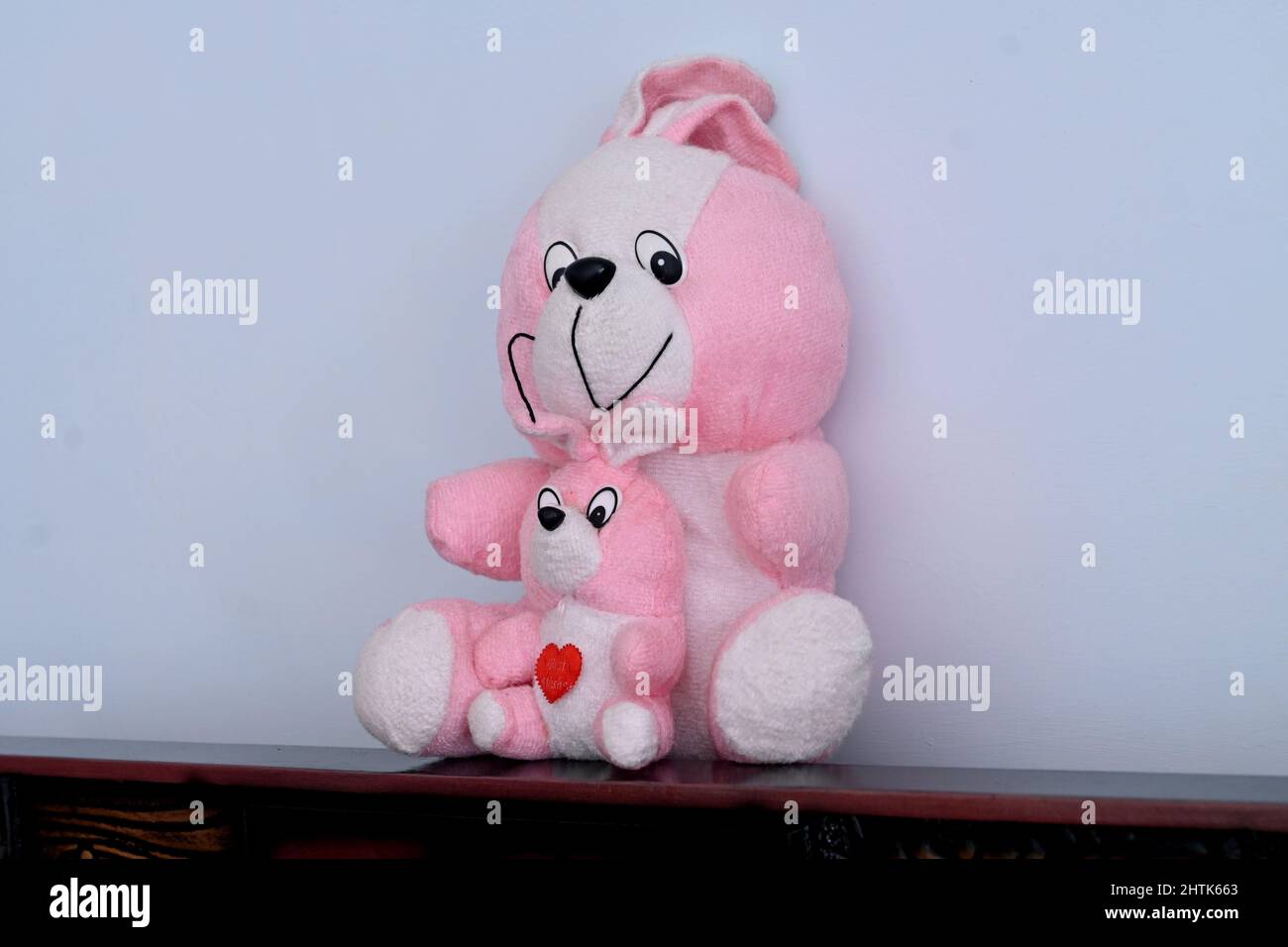 Nahaufnahme des wunderschönen rosa weißen Teddybären, der auf einem braunen Tisch über einem weißen Hintergrund sitzt. Stockfoto