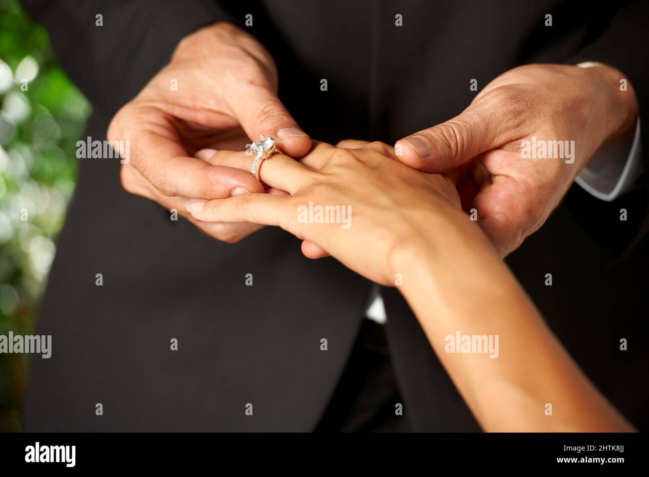 Ihre Liebe verpfänden. Beschnittene Ansicht eines Bräutigams, der einen Ring auf seinen Bräute-Finger rutscht. Stockfoto