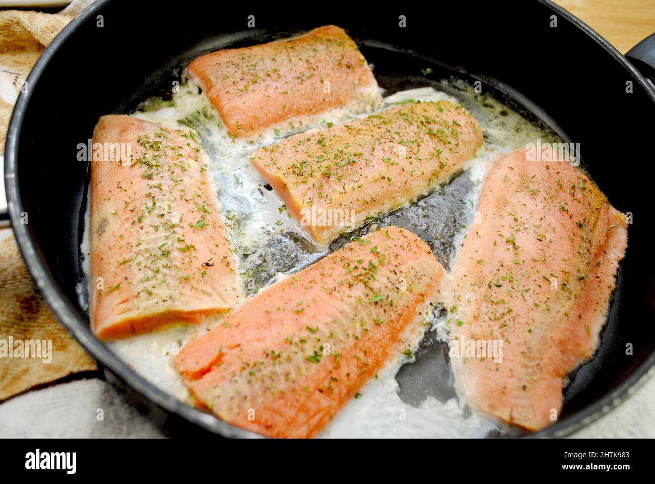 Lachs, der in Knoblauch, Petersilie, Pfeffer und Butter in einer Pfanne ansaut Stockfoto