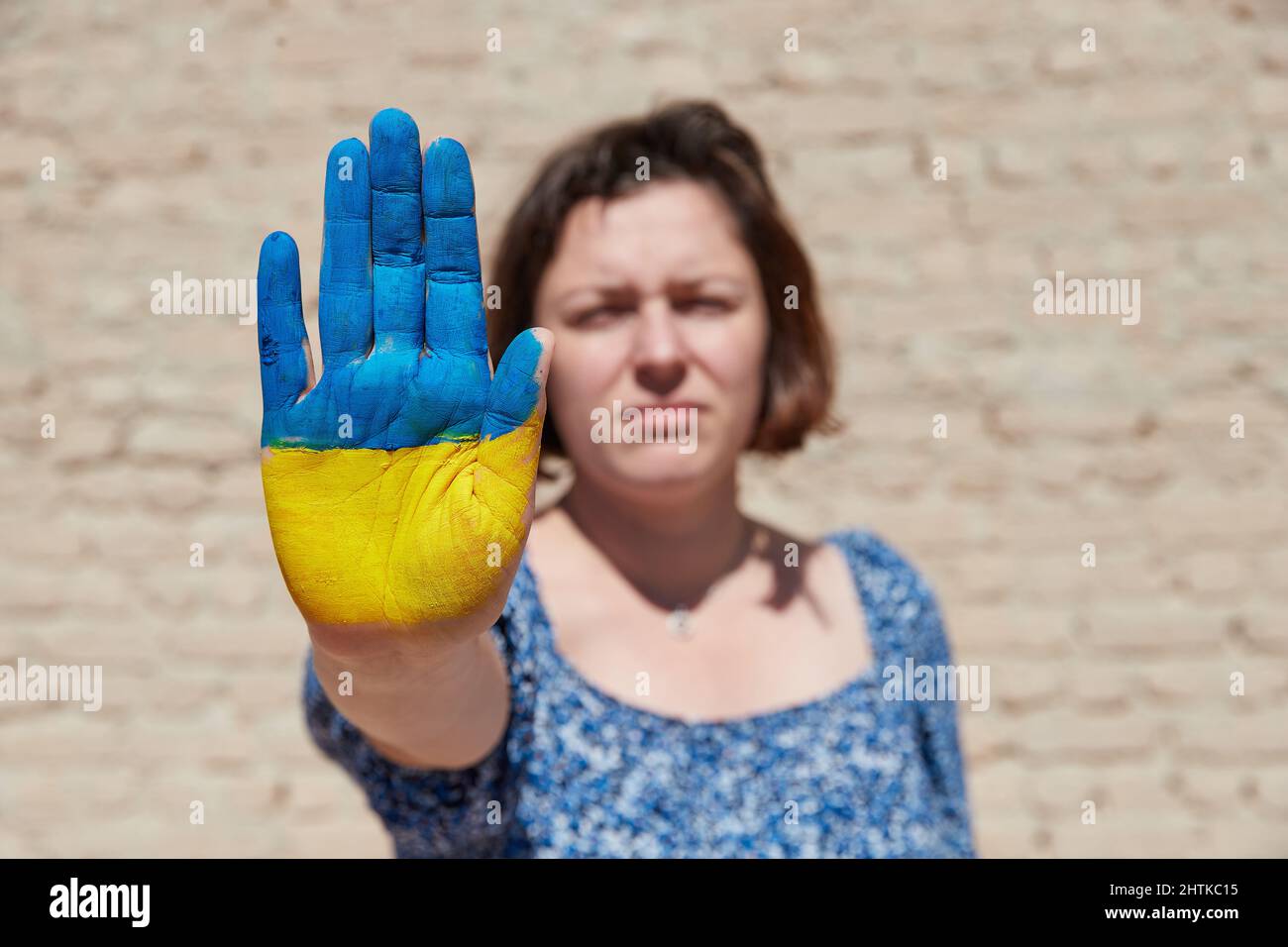 Ukrainische Frau mit einem Flaggensymbol auf der Hand zeigt ein Stoppschild am blauen Himmel. Krieg beenden Stockfoto