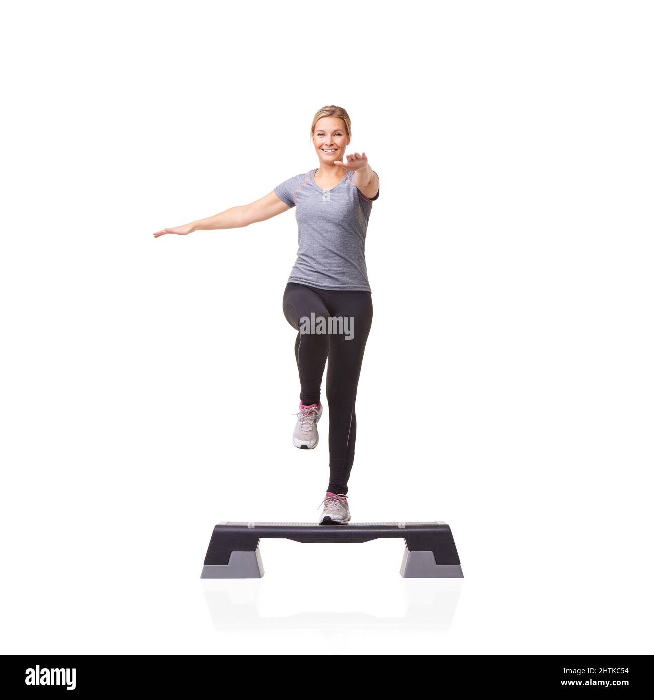 Ihre Gesundheit Schritt für Schritt verbessern. Eine lächelnde junge Frau, die auf einem Aerobic-Schritt vor weißem Hintergrund Aerobic macht. Stockfoto