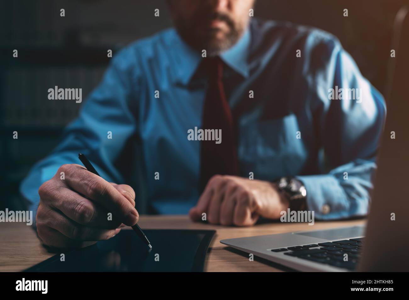 Geschäftsmann, der spät in der Nacht elektronische Unterschrift mit digitalisiertem Stift und Pad im dunklen Büro unterschreibt, selektiver Fokus Stockfoto