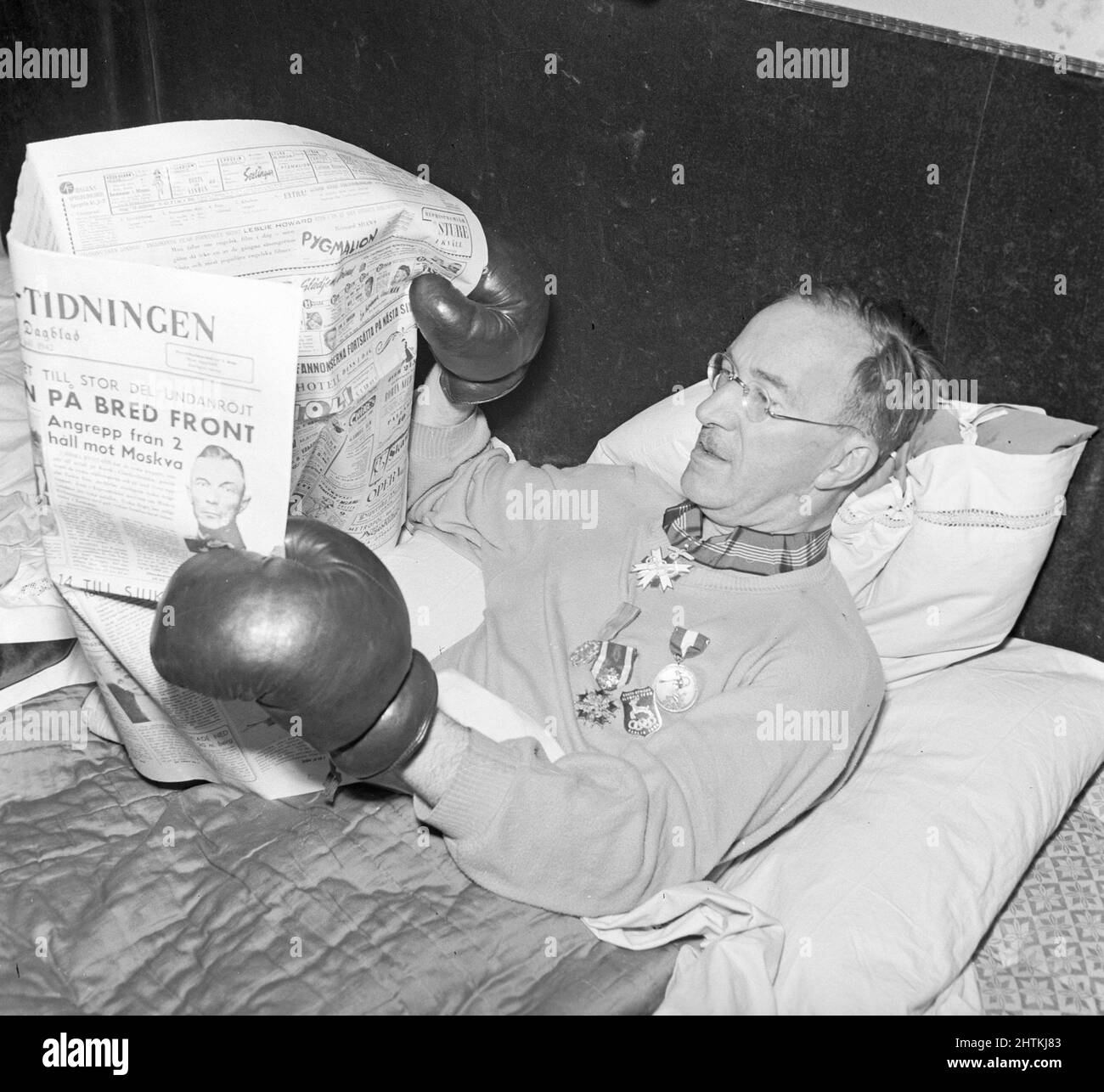 Gökar Well. Richtiger Name Oscar Söderlund Sportjournalist. 1892-1965 im Bett abgebildet und liest das Papier und hält es mit seinen Boxhandschuhen. Schweden 1943 Kristoffersson Ref. C80-3 Stockfoto