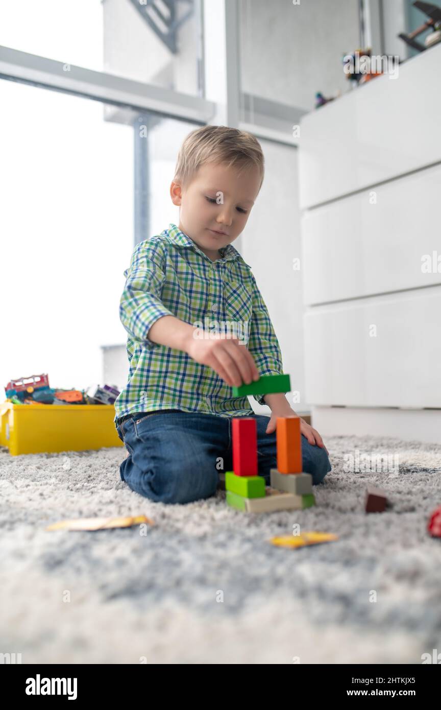 Kreativer kleiner Junge, der aus Spielzeugblöcken eine Gebäudestruktur konstruiert Stockfoto
