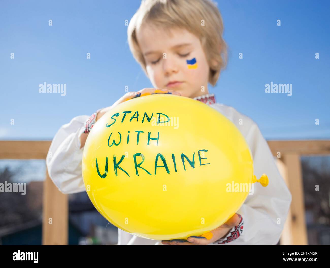 Defokusstes Kind hält in den Händen gelben Ballon mit Aufschrift Stand mit Ukraine. Solidarität mit der Ukraine. Hilferuf und Unterstützung der Militärischen Konferenz Stockfoto