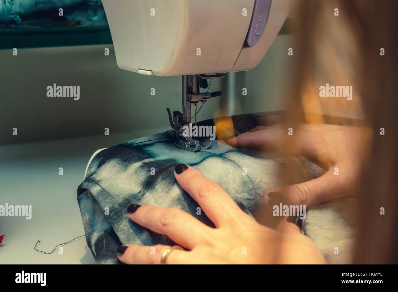 Nahaufnahme Rückansicht der kaukasischen Frau, die blaue Stoffe auf Nähmaschine näht, Textilkonzept, Bild mit Kopierraum. Stockfoto