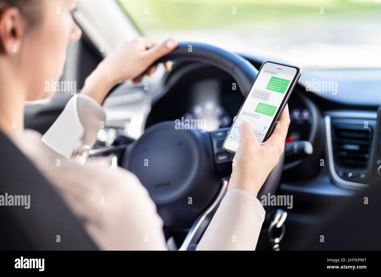 Verwenden des Telefons während der Fahrt mit dem Auto. Abgelenkter Fahrer schreibt im Fahrzeug. Unverantwortliche Frau, die SMS-Nachrichten mit dem Mobiltelefon im Verkehr überprüft. Stockfoto