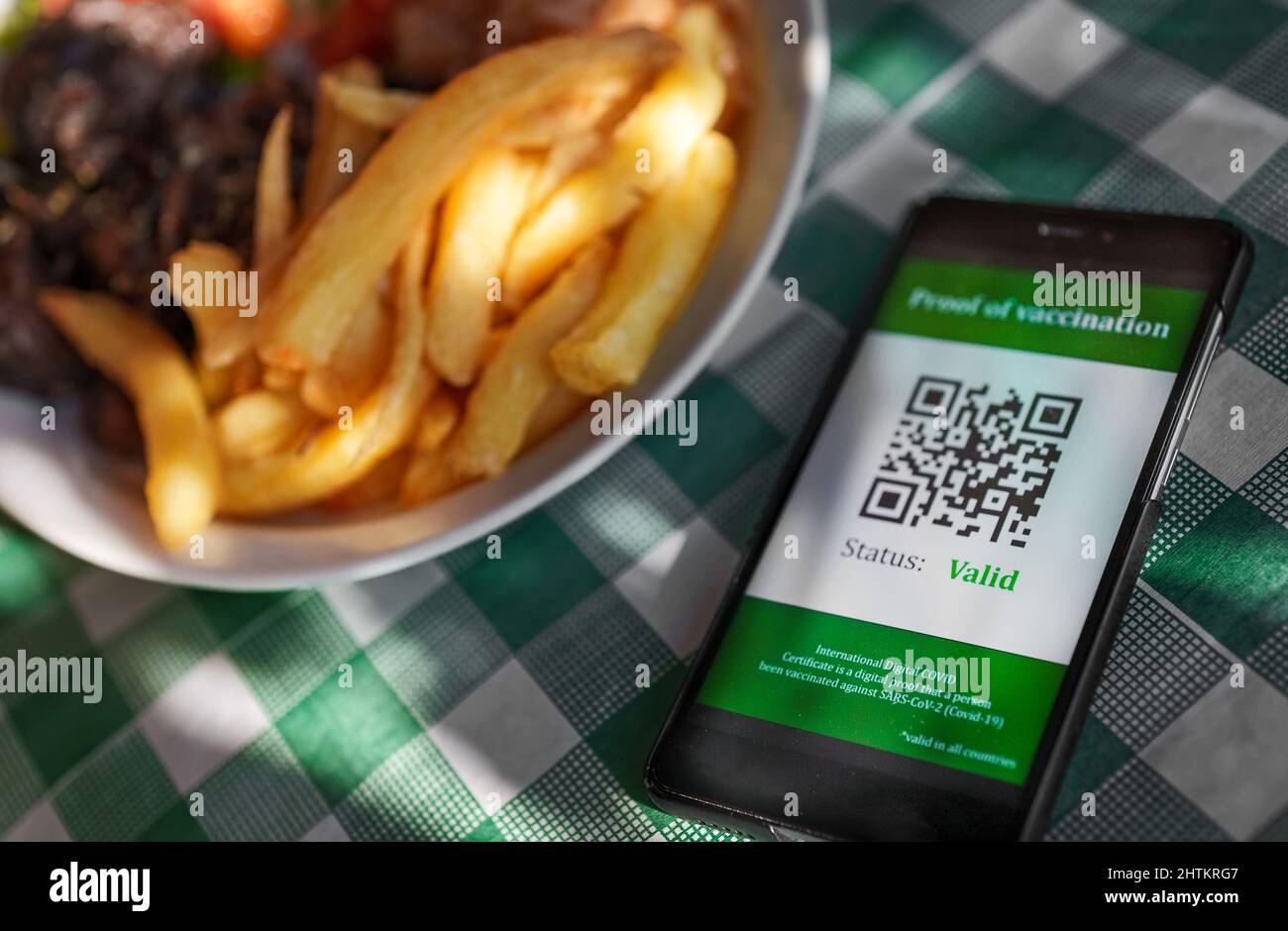 Frau im Restaurant mit Immunisierungszertifikat auf dem Smartphone. Status ist gültig. Stockfoto