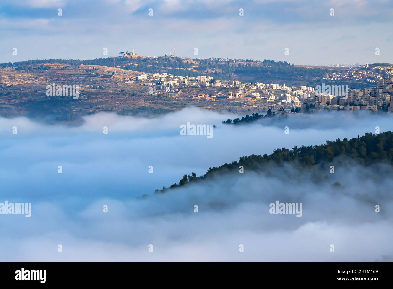 Eine niedrige Wolke in einem Tal zwischen den Judäa-Bergen, unterhalb der Dörfer und Städte um Jerusalem, Israel, bei Sonnenaufgang. Stockfoto