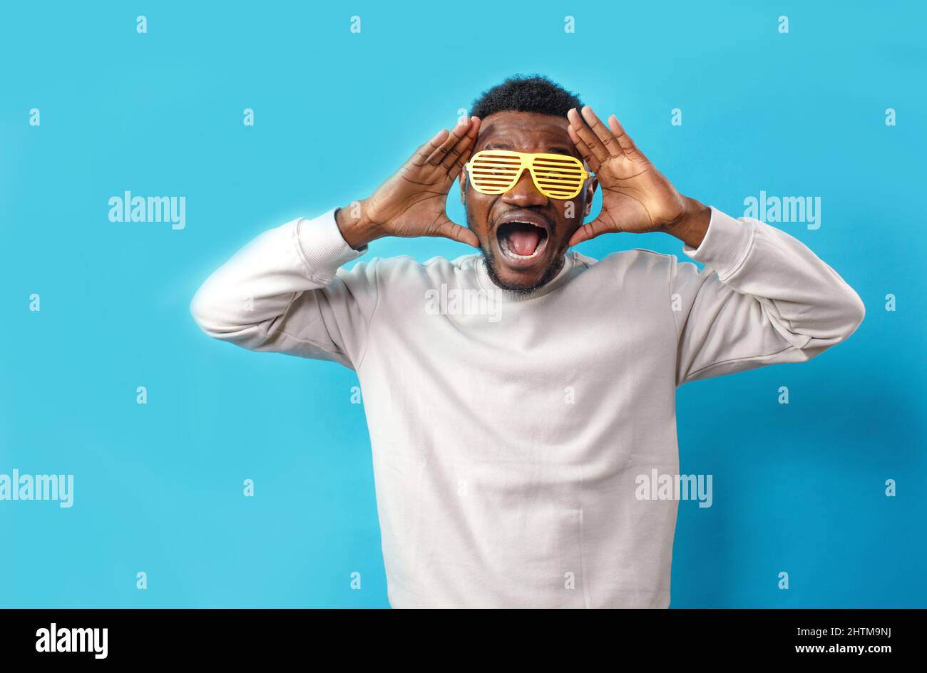 Ein Bild eines schwarzen Mannes in einer gelben, modischen Brille, der Schock und Verzweiflung ausdrückt, seinen Kopf mit beiden Händen berührt und mit breitem Mund schreit Stockfoto