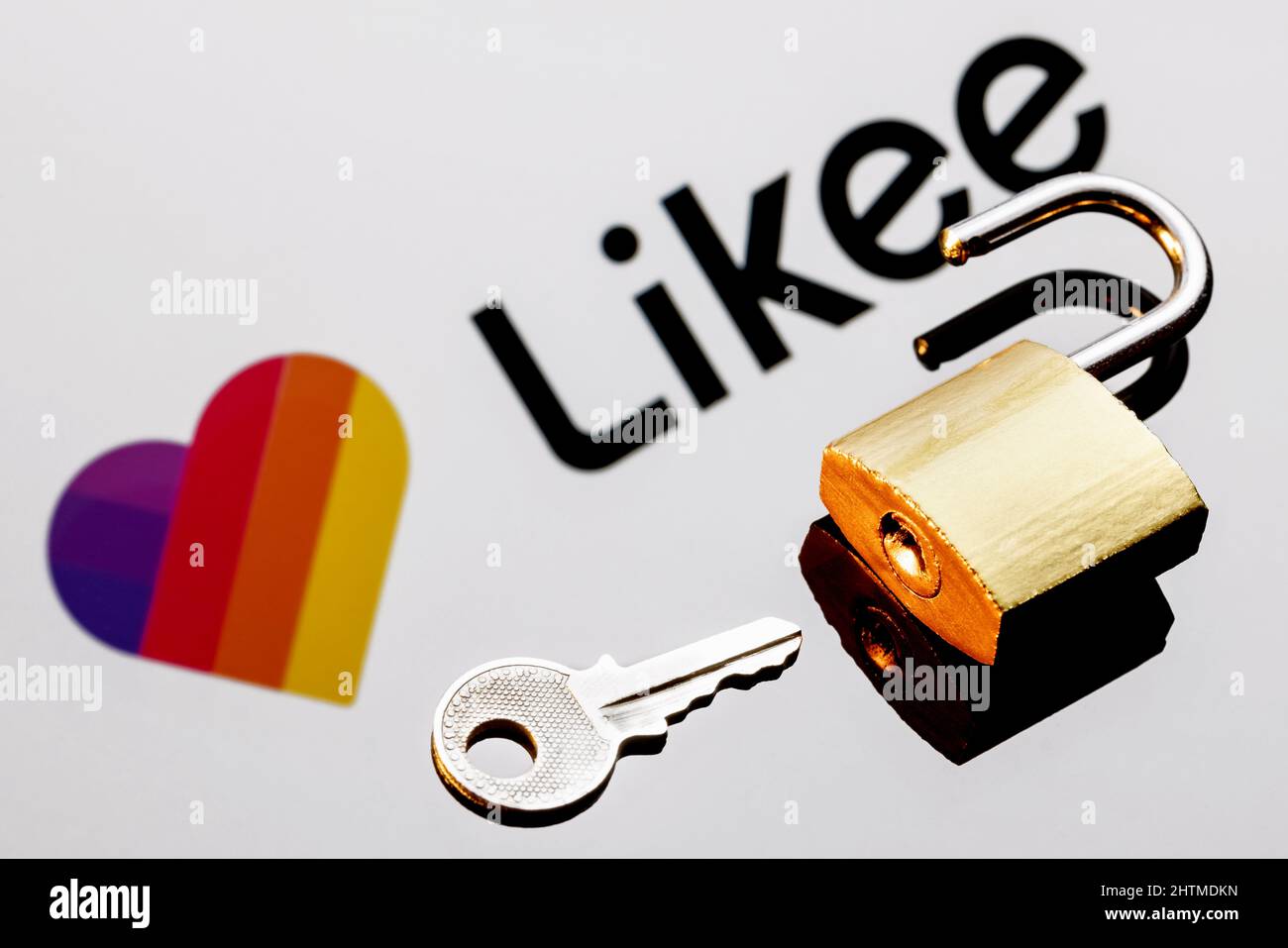 Ein offenes Sicherheitsschloss und Schlüssel auf dem Hintergrund des Likee Short Video Sharing Service Logos in Spiegelreflexion. Stockfoto