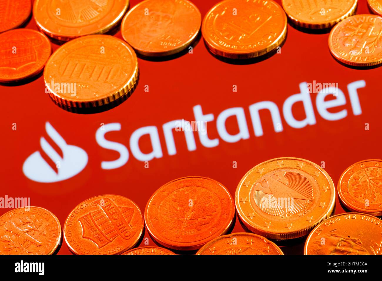 Verschiedene Metallmünzen auf dem Hintergrund des Santander Banklogos Stockfoto