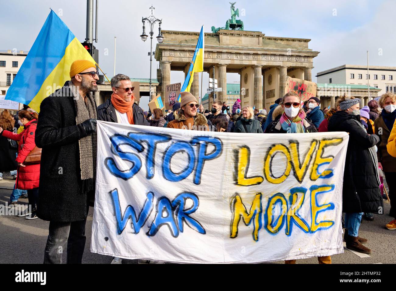 Menschen mit Plakaten nehmen an einem Protest gegen den Krieg in der Ukraine in der Nähe des Brandenburger Tors Teil. Text Stop war Love Mehr zu Textilien. Stockfoto