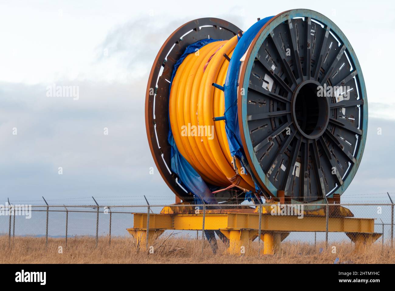 Bulk-Sub-Sea-Glasfaser-Kabel auf einer Metallspule auf einem Schiffsständer. Die orangefarbene Datenleitung ist im Speicher um eine schwarze Rolle gewickelt. Stockfoto