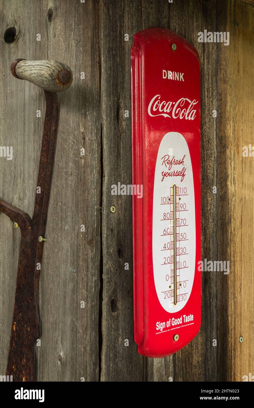 Antikes Coca Cola Thermometer aus Metall an der Außenwand einer alten rustikalen Holzdiele-Kabine. Stockfoto