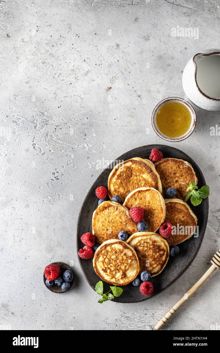 Pfannkuchen in Keramikplatte mit Beeren, Minzblättern, Soße Boote und Honiglöffel, Draufsicht Stockfoto