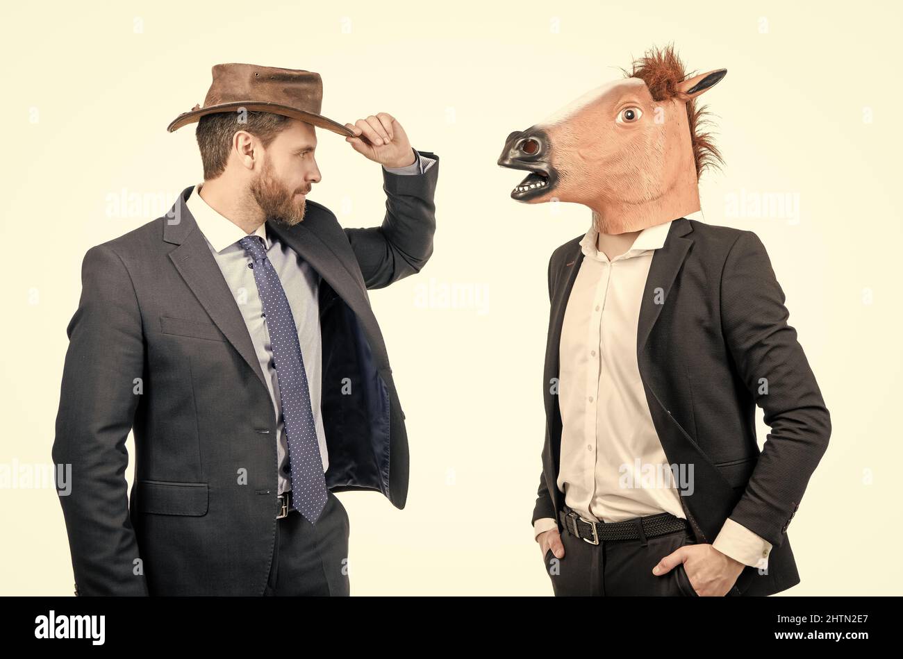 Cowboy Mann und Geschäftsmann in Pferdekopfmaske auf Kostümfest, Corporate Halloween Stockfoto