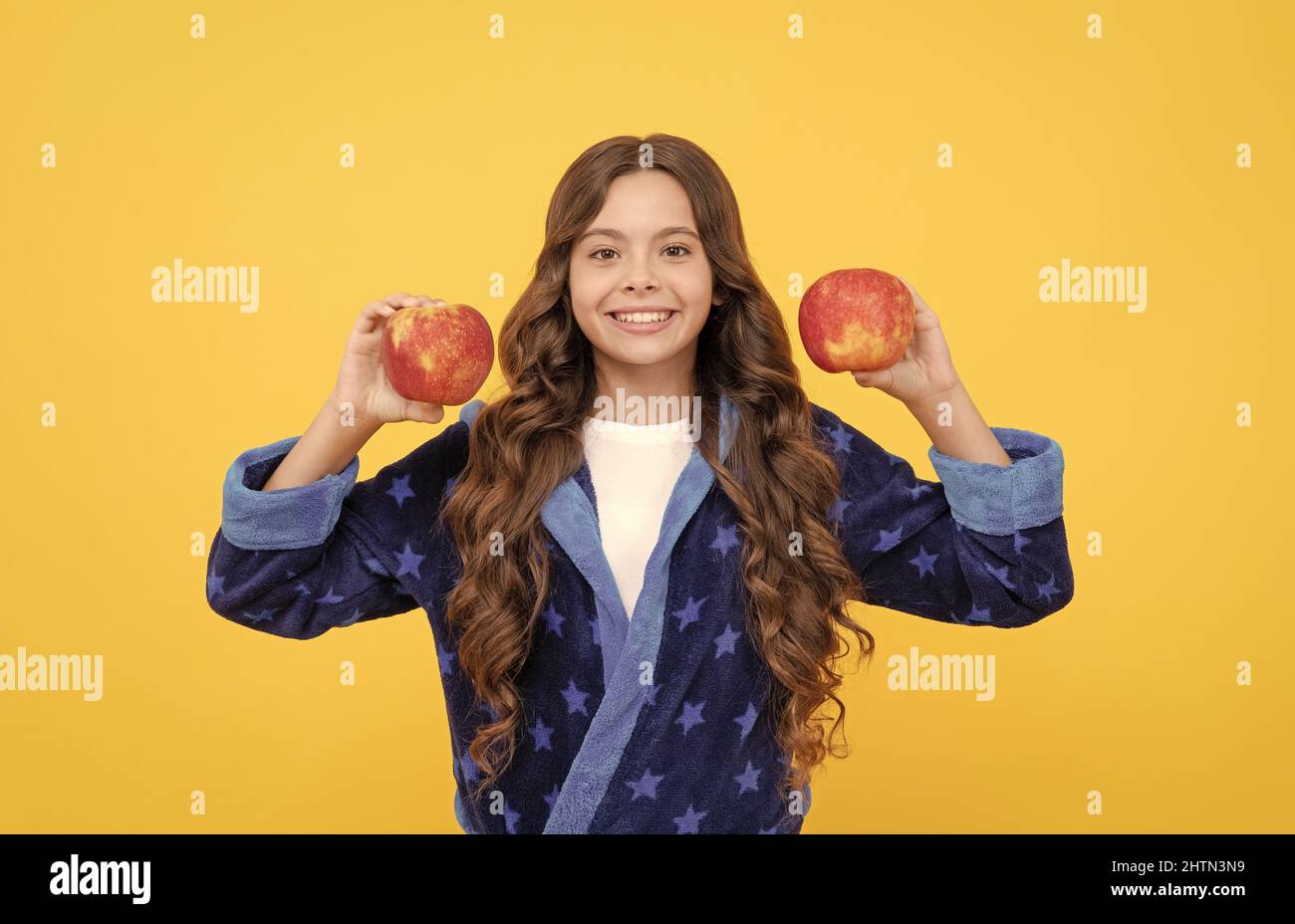 Fröhliche Teenager-Mädchen mit lockigen Haaren in komfortablen Pyjama gehen, um gesunde Apfel, Vitamin essen Stockfoto