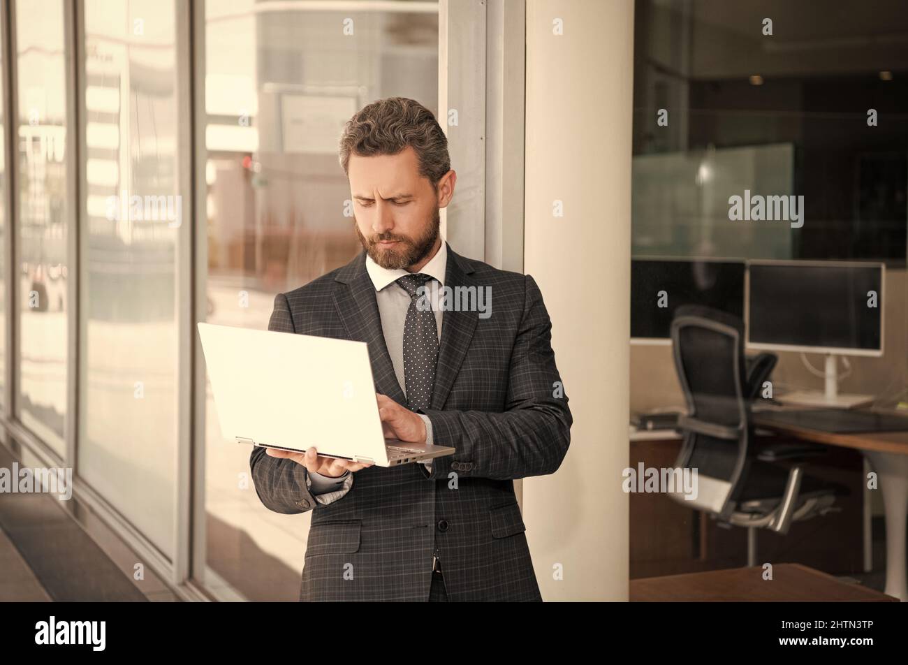 Bärtiger, reifer Mann im Anzug, der in einem Geschäftsbüro einen Laptop verwendet, agiles Geschäft Stockfoto