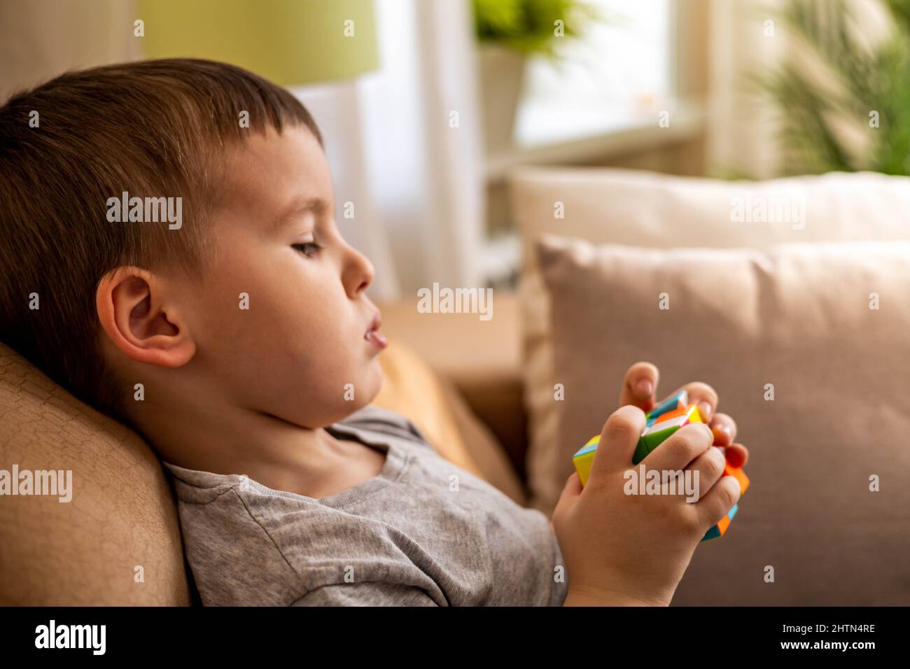 Niedlichen Baby Junge Montage bunten Rubik Würfel lösen logische Spiel auf der Couch zu Hause liegen Stockfoto