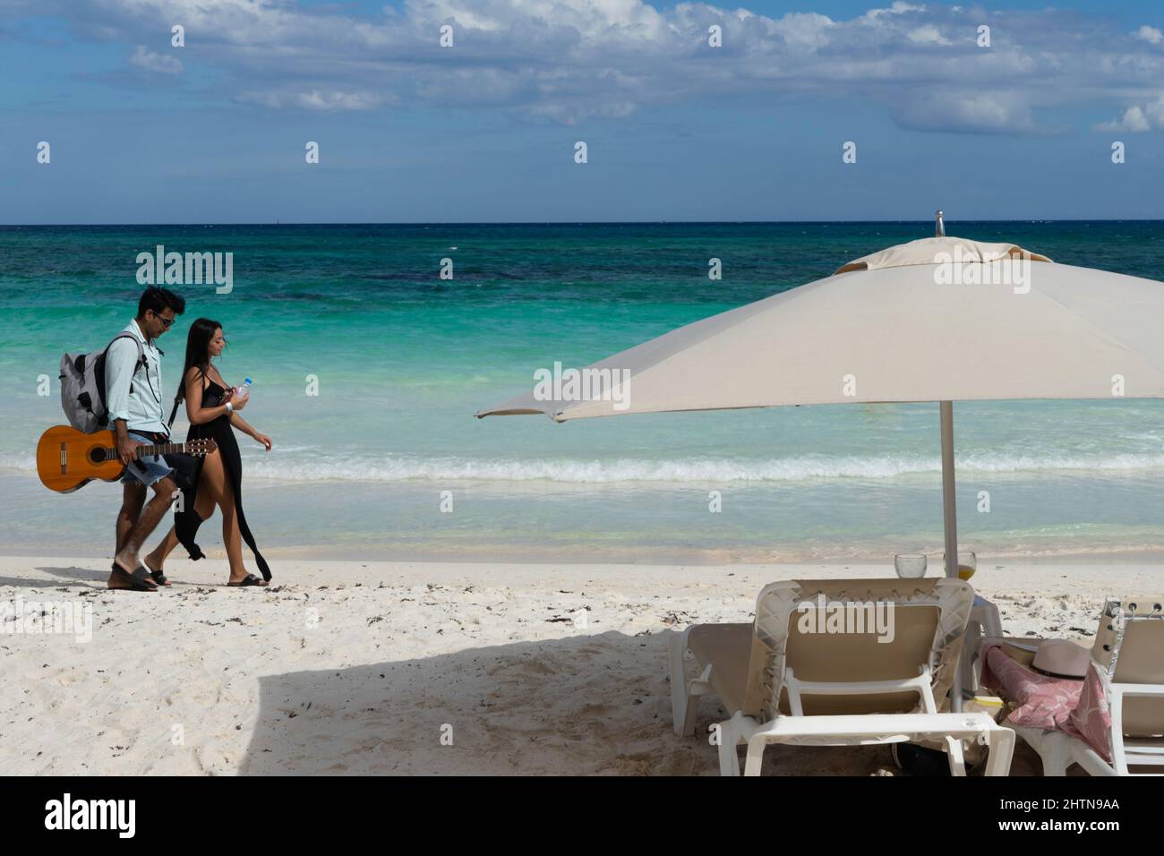 Ein Sonnenschirm im Vordergrund und ein Mann und eine Frau, die mit Gitarre in der Hand in Mexiko laufen Stockfoto
