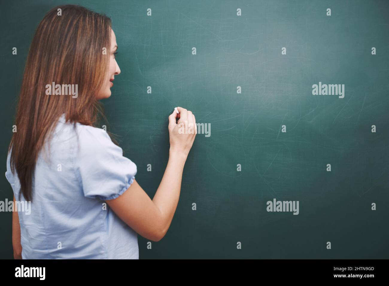 Die Lektion für heute ist Eine hübsche junge Lehrerin, die heute einen Stundenplan auf die Tafel schreibt. Stockfoto