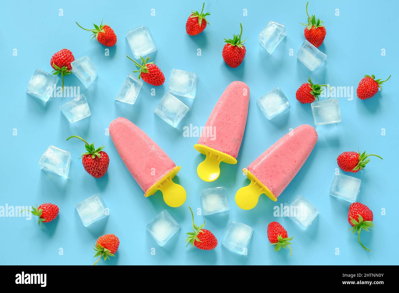Hausgemachte Eiszapfen. Natürliches Eis in hellen Plastikformen, Erdbeeren und Eiswürfel auf blauem Hintergrund. Draufsicht Flat Lay. Stockfoto