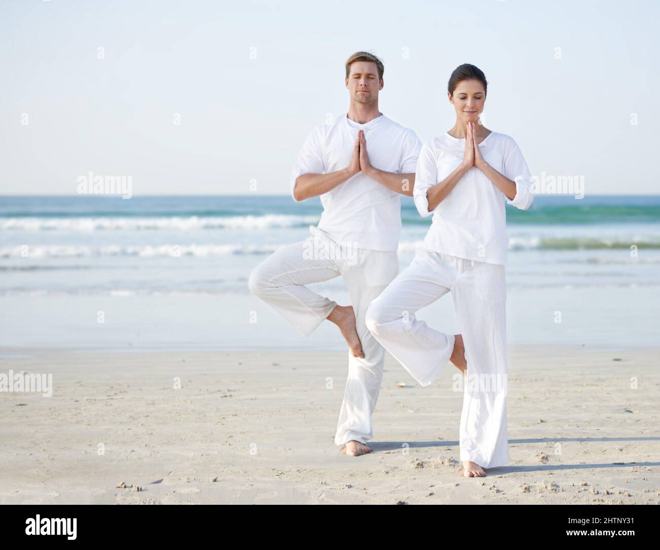 Yoga am Meer. Ein junges Paar, das am Strand Yoga praktiziert. Stockfoto