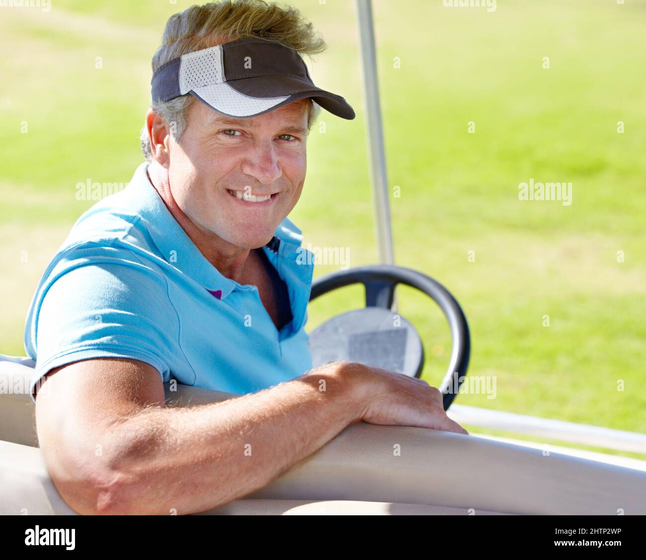Auf dem Weg zum nächsten Grün. Porträt eines lächelnden, reifen Golfspielers, der in einem Golfwagen sitzt. Stockfoto