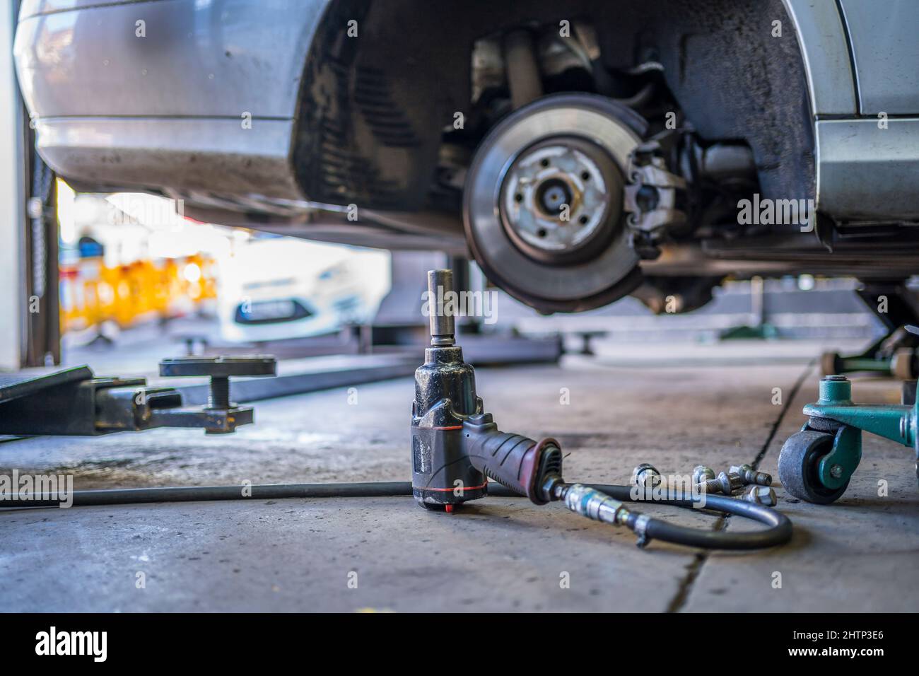 Ein Fahrzeug, das in einer Garage auf einem Wagenheber angehoben wurde, wobei das Rad entfernt wurde und ein Luftaufprallschlüssel im Vordergrund stand. Stockfoto