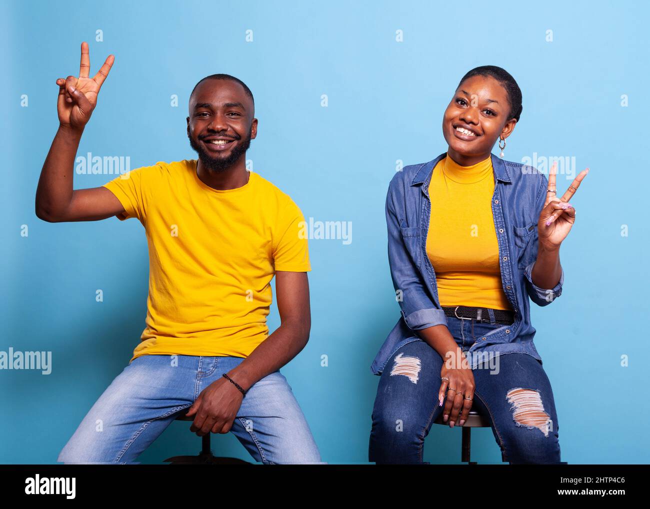 Glückliches Paar lächelt und zeigt ein Friedenszeichen mit den Fingern vor der Kamera. Fröhlicher Freund und Freundin tun optimistische Geste mit Händen im Studio. Angeregte Partner, die V-Symbol machen Stockfoto