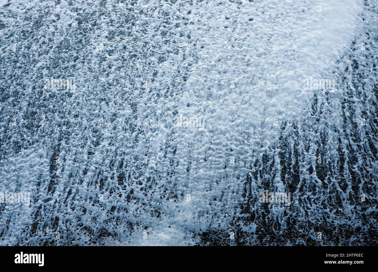 Übersicht über Meerwasserschaum am Kiesstrand Stockfoto