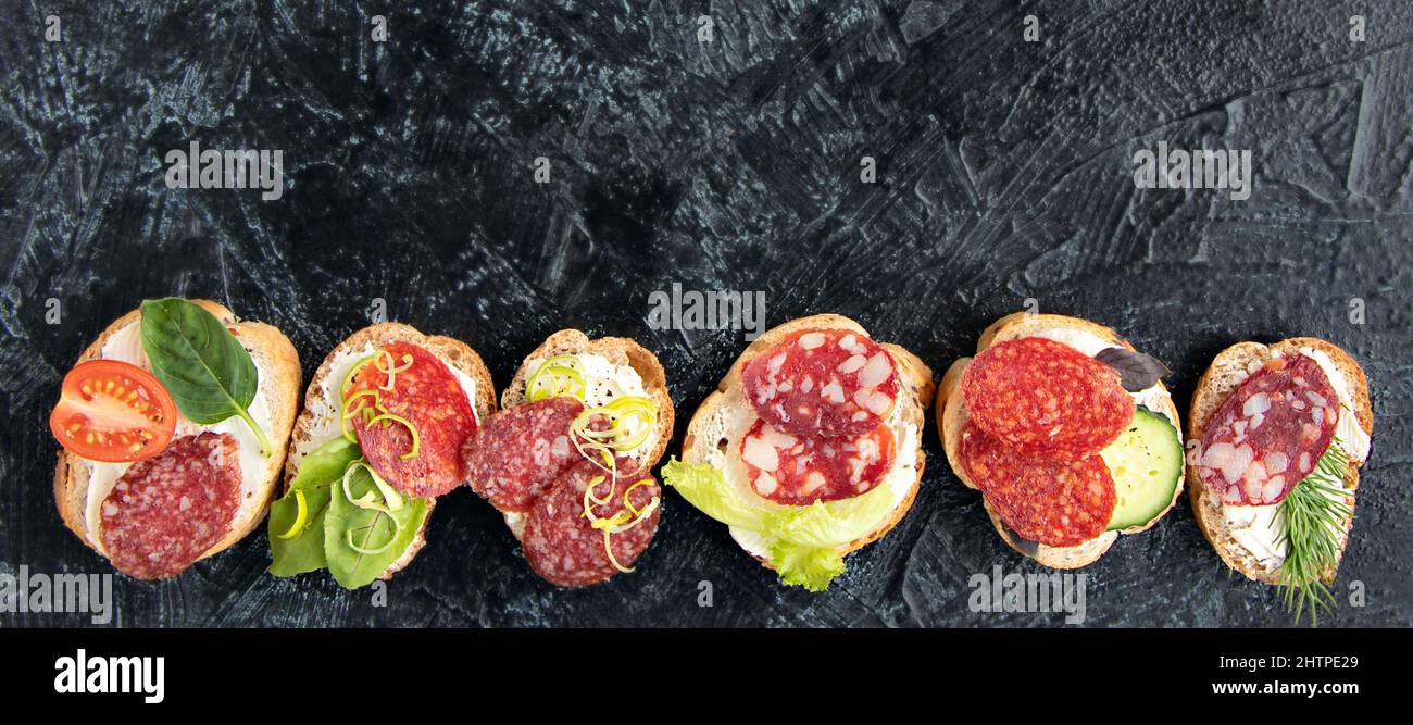 Banner mit flachem Lay mit Sandwiches mit Wurst, Frischkäse, Tomaten, Dill, Gurken, Und Basilikum. Serviert einen Snack für Vorspeisen auf schwarzem Hintergrund mit Kopierplatz. Draufsicht Stockfoto