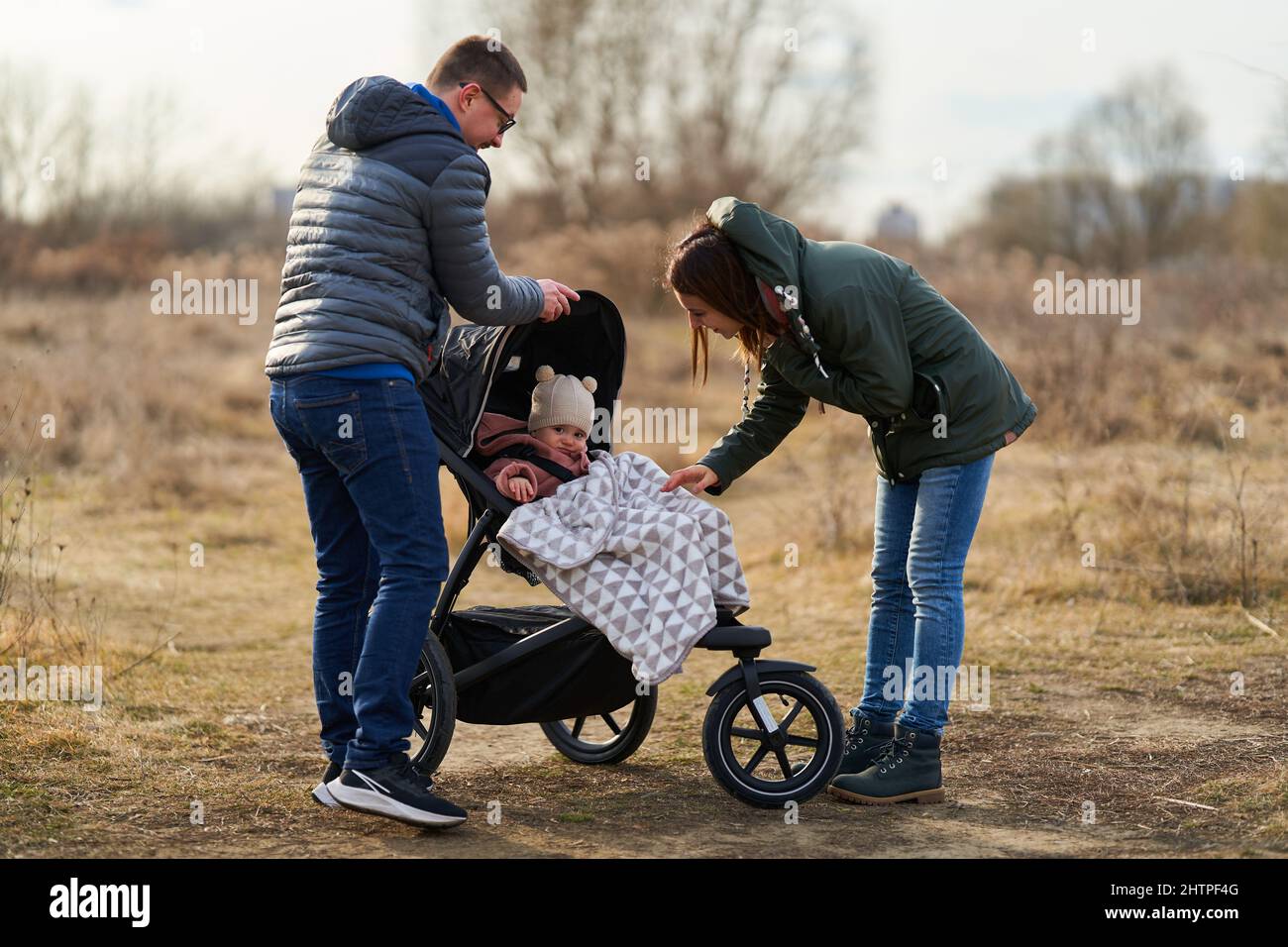 Junge Familie mit ihrem kleinen Mädchen, die mit dem Kinderwagen durch den Park in einem Wohngebiet spazierengeht Stockfoto