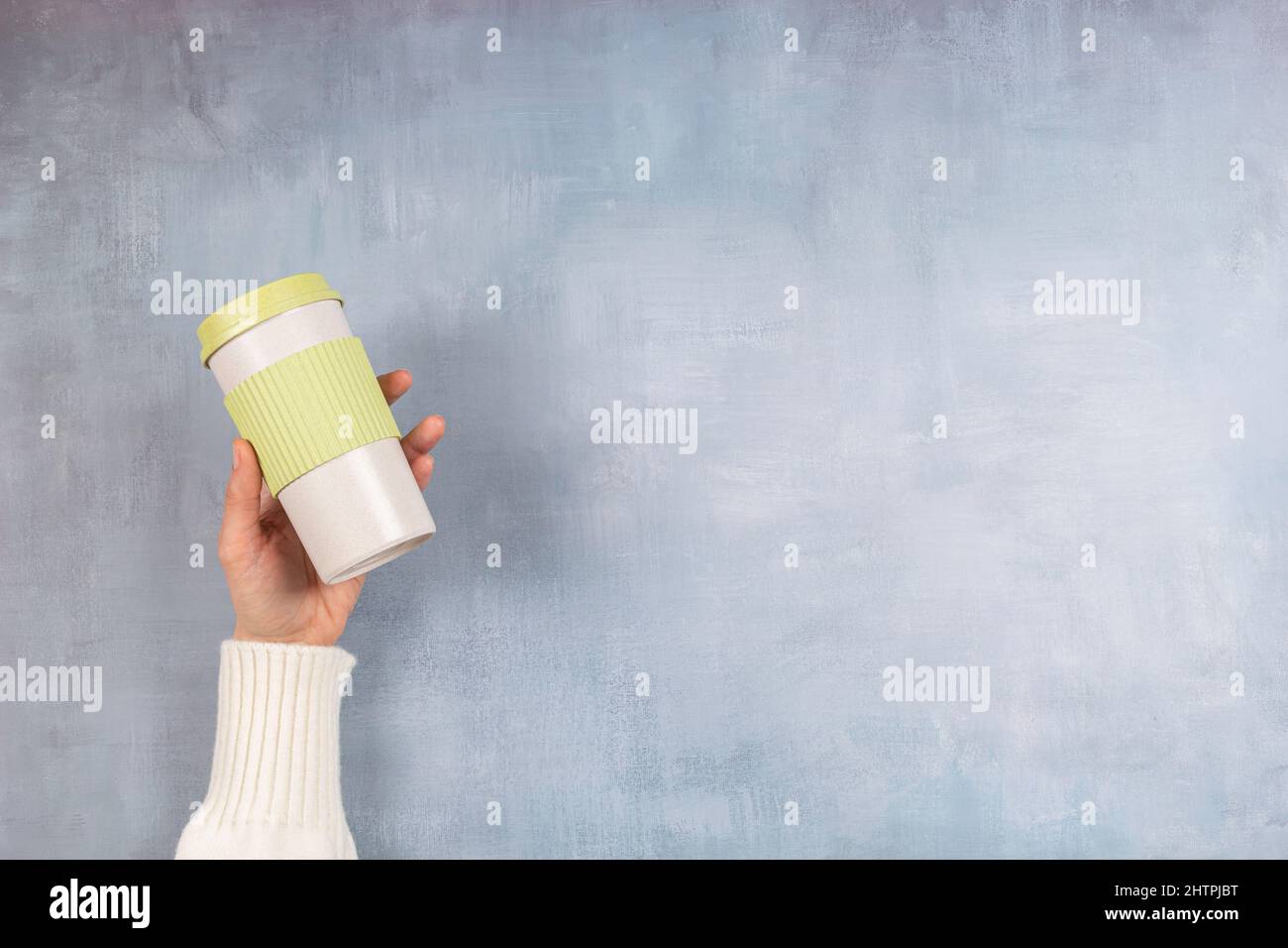 Nachhaltiges Wohnen, keine Verschwendung, kein Kunststoffkonzept. Weibliche Hand hält stilvolle wiederverwendbare umweltfreundliche Kaffeetasse auf grauem Hintergrund Stockfoto
