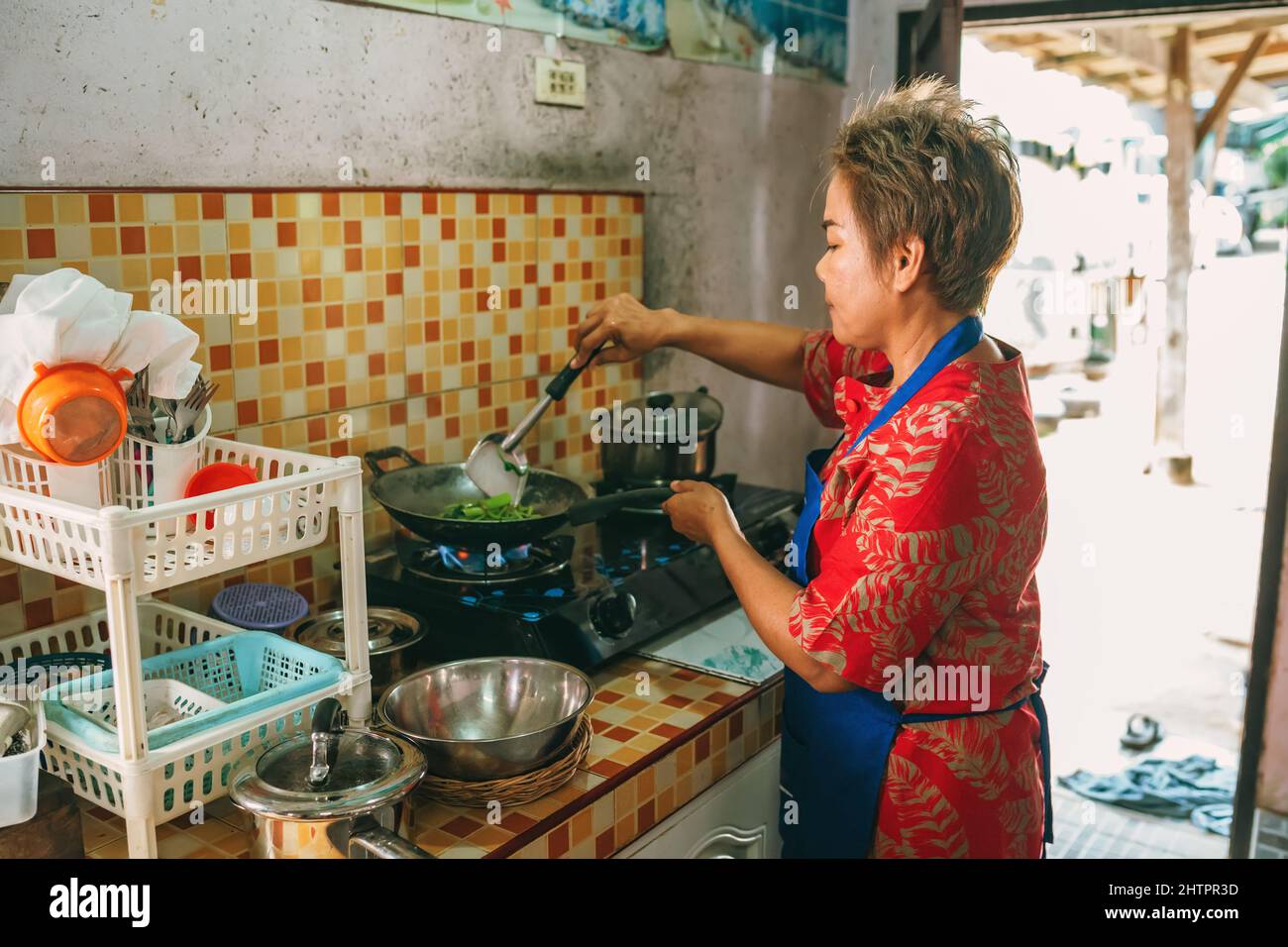 Asiatische Frau kurze Haare in roten Kleid Kochen rühren gebratenes Gemüse in der Küche Stockfoto