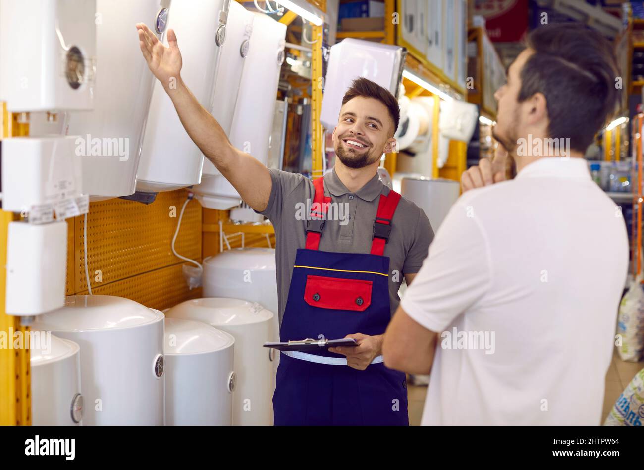 Lächelnder Verkäufer, der einem Kunden Kessel und Warmwasserbereiter zeigt, die er im Laden hat Stockfoto