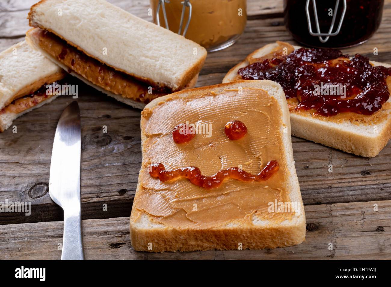 Anthropomorphes Gesicht auf Brot mit Erdnussbutter am Tischmesser, Sandwiches und Gläser auf dem Tisch Stockfoto