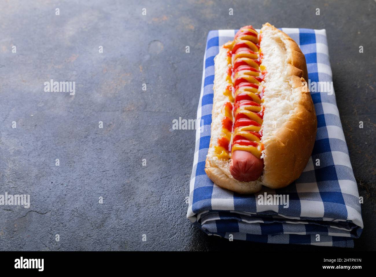 Nahaufnahme von Hot Dog mit Tomate und musterter Sauce auf karierter Serviette am Tisch Stockfoto
