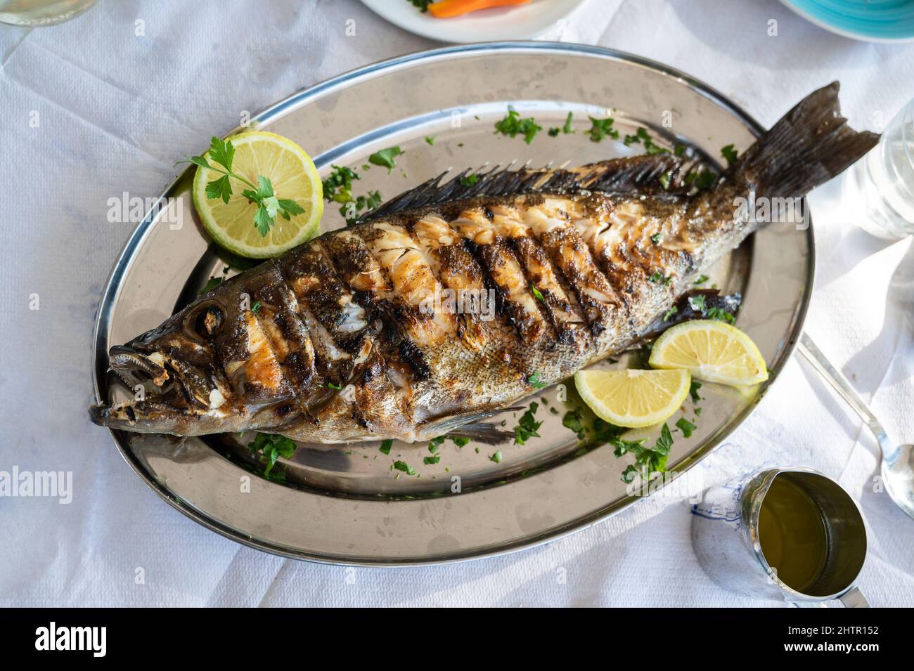 Gegrillter Zackenbarsch auf einem Silberteller in einem Restaurant auf Kreta, Griechenland. Gebackene Fisch dekoriert Ende serviert in einem Fisch-Restaurant in Kreta, Griechenland ist Serv Stockfoto
