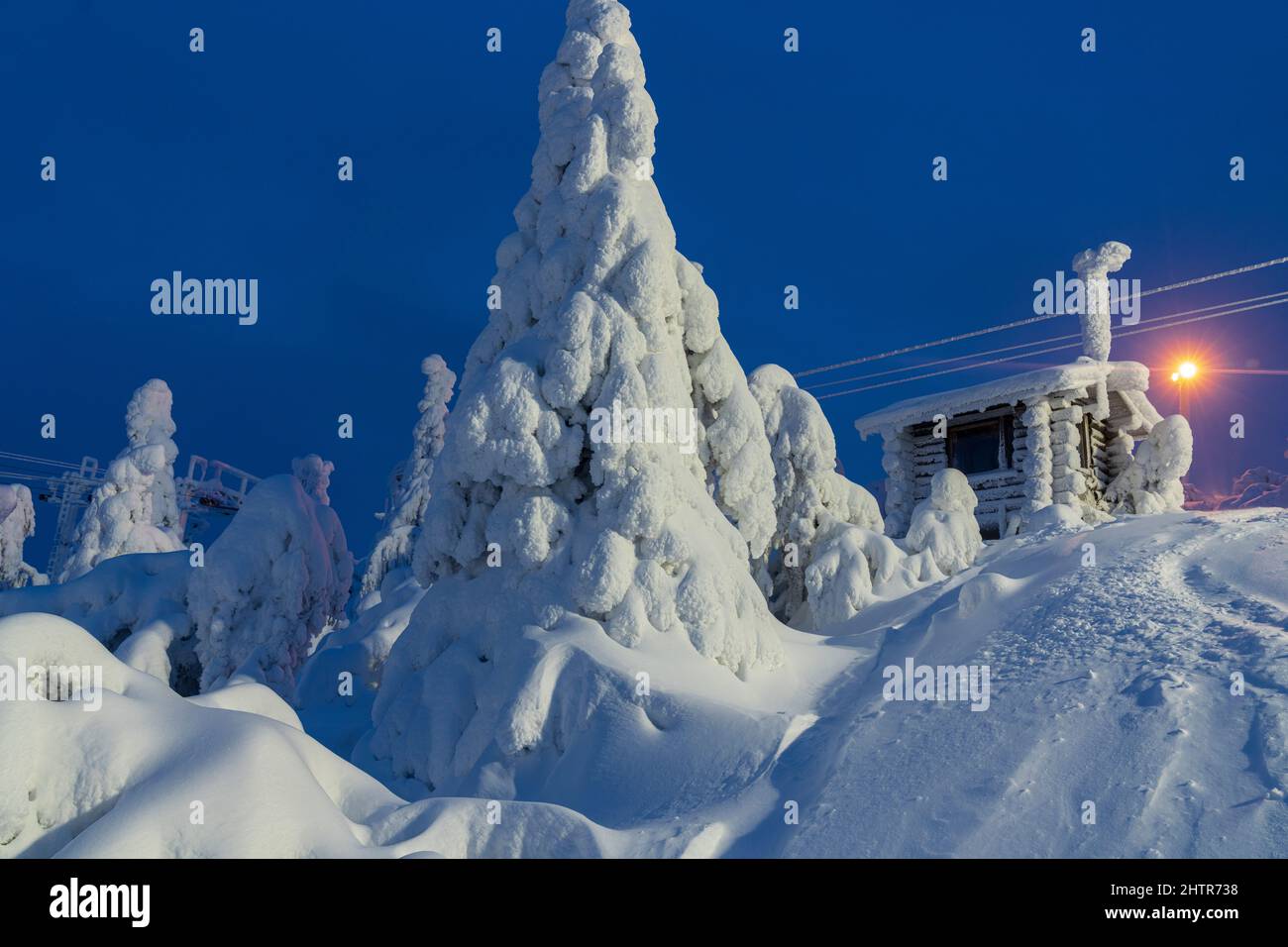 In der gefrorenen Landschaft des Skigebiets ISO-Syote, Lappland, Finnland, befinden sich Holzhütten und Fichten, die mit Schnee bedeckt sind Stockfoto