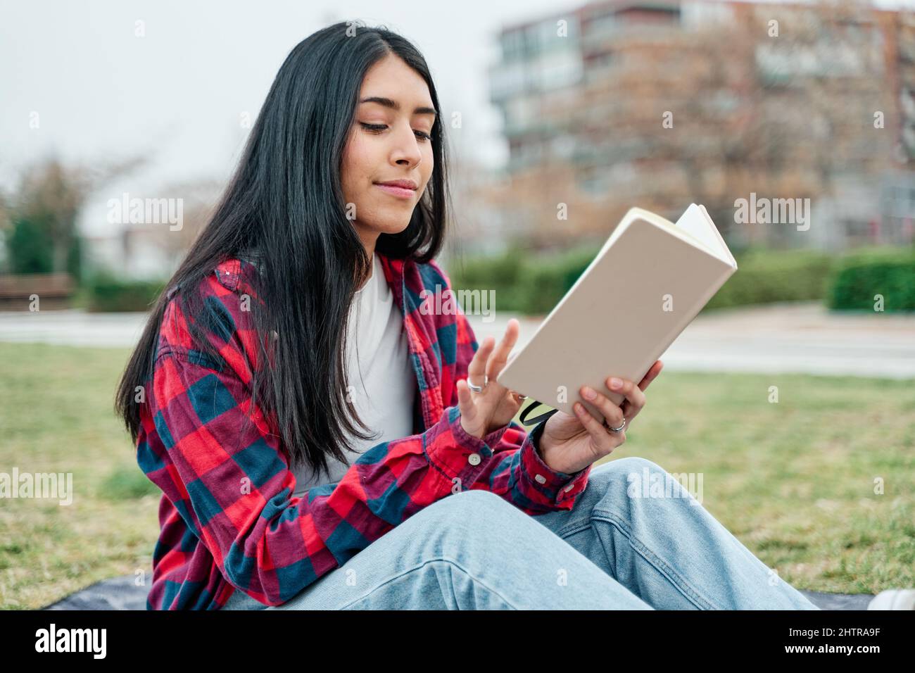 Junge lateinische Mädchen sitzt in einem Stadtpark Lesen eines Buches. Konzept der Städtereise und Freizeit. Stockfoto