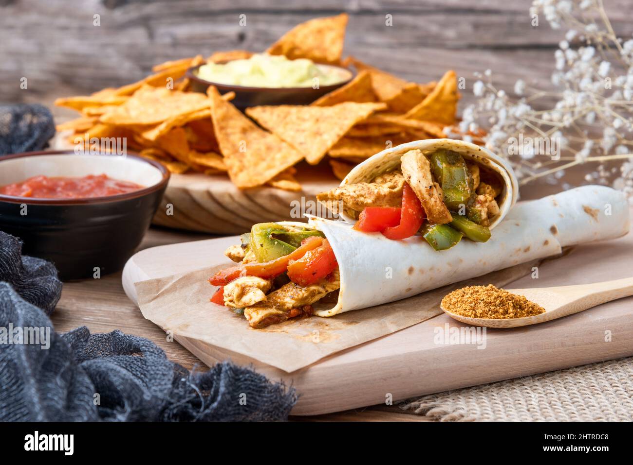 Nahaufnahme von Chicken Fajitas mit Paprika, Zwiebeln und Gewürzen und Guacamole-Sauce mit Tortilla-Chips oder Nachos auf einem Holztisch Stockfoto