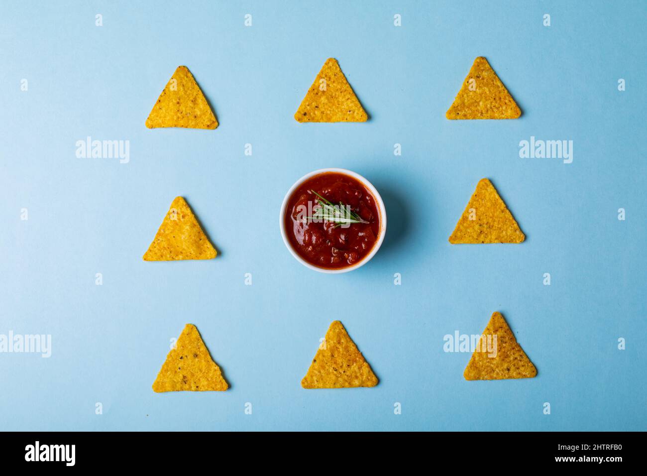 Blick von oben auf rote Sauce mit Rosmarin inmitten von Nacho-Chips auf blauem Hintergrund Stockfoto