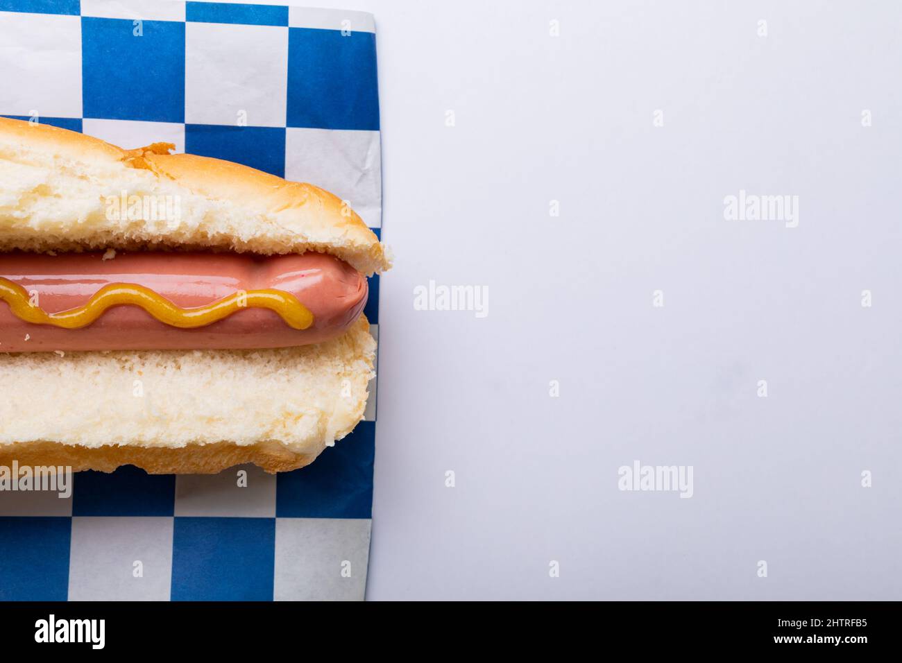 Hot Dog mit musterter Sauce auf kariertem Musterpapier auf weißem Hintergrund mit Kopierfläche Stockfoto