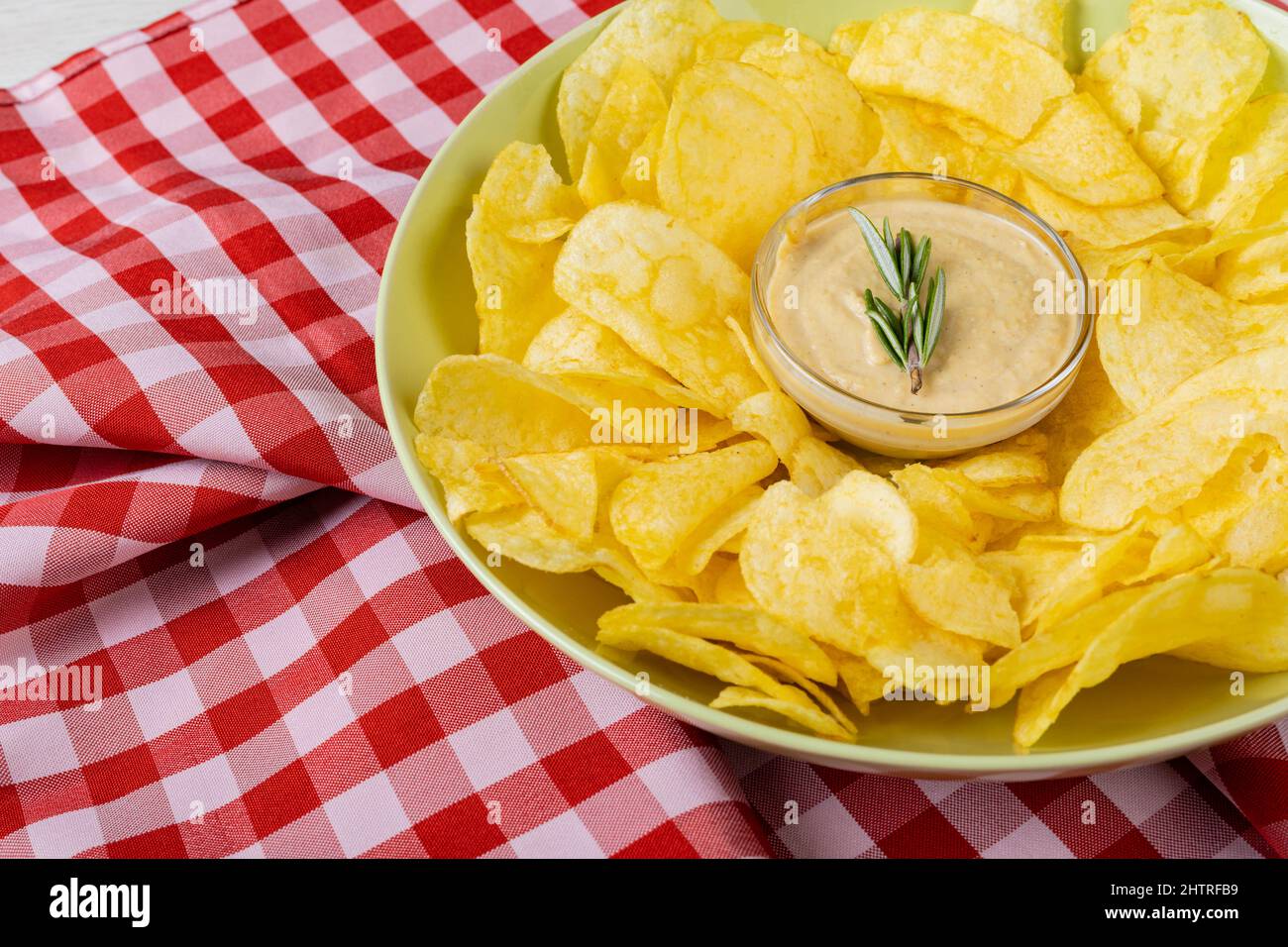 Nahaufnahme der Sauce inmitten von Kartoffelchips, die auf dem Teller auf karierter Serviette am Tisch serviert werden Stockfoto